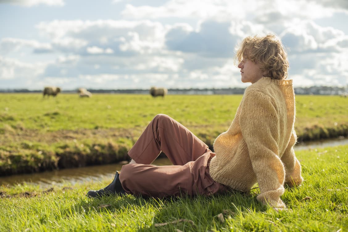 A man sitting on the grass and wearing human hair sweater 
