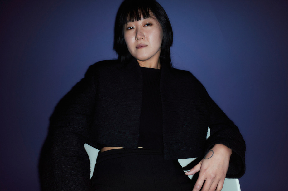 A woman sitting on a chair and wearing black human hair blazer